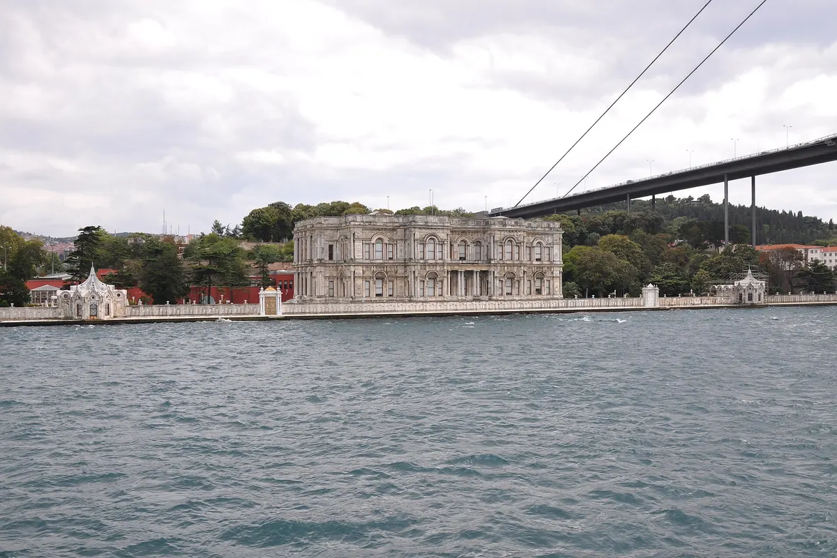 Beylerbeyi Palace on the Asian shore, a pale stone building with columns, seen across the water with the bridge rising behind it.