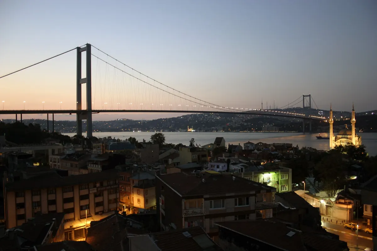 The Bosphorus Bridge strung with lights at dusk, with the domed Ortaköy Mosque lit on the shore on the right.